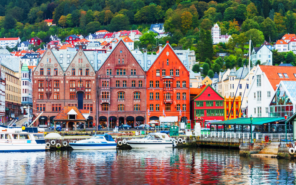 Bunte H&auml;user am Hafen von Bergen mit Booten im Vordergrund und gr&uuml;nen H&uuml;geln im Hintergrund.
